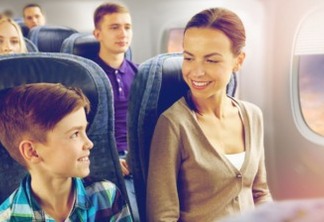 a imagem apresenta uma mãe e seu filho sentados dentro de um avião, eles estão lado a lado sorrindo um para o outro.