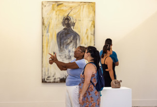 Vânia Rosa da Silva, pedagoga e intérprete de Libras, em frente a uma tela, se comunicando com uma visitante do museu