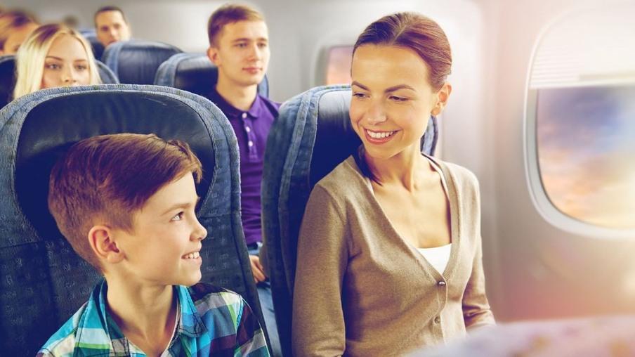 a imagem apresenta uma mãe e seu filho sentados dentro de um avião, eles estão lado a lado sorrindo um para o outro.