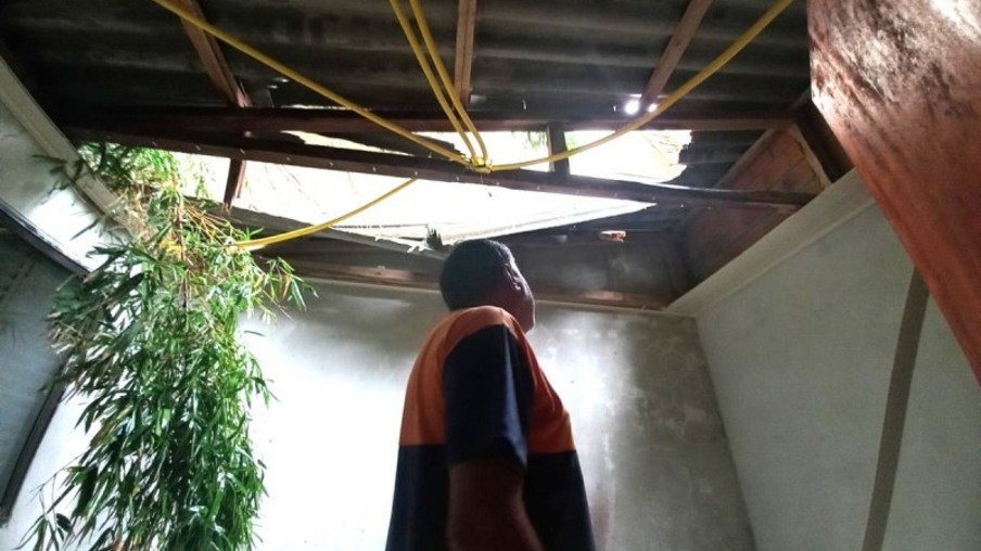 Servidor da Defesa Civil de Santa Maria olha para danos em telhado de residência.