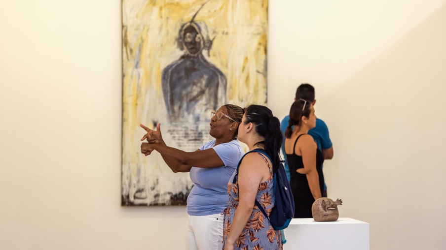 Vânia Rosa da Silva, pedagoga e intérprete de Libras, em frente a uma tela, se comunicando com uma visitante do museu