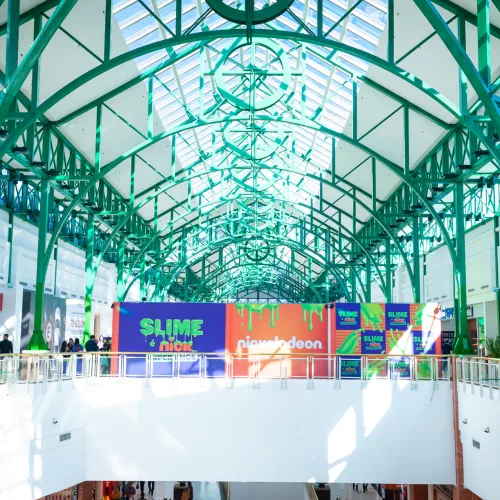 Área superior do shopping, com arcos em ferro verde, e no andar de cima tapumes com a inscrição do nome do evento - Slime é Nick Experience.