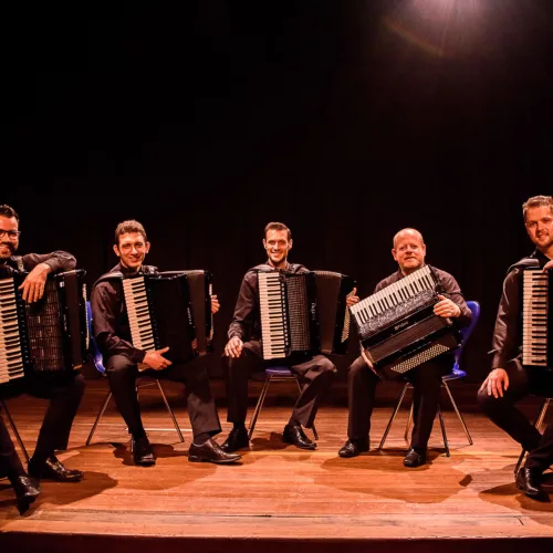 Cinco músicos, sentados, com seus acordeons