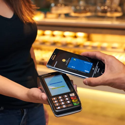 Uma pessoa aproxima um celular de outra com uma máquina de pagamento Visa.