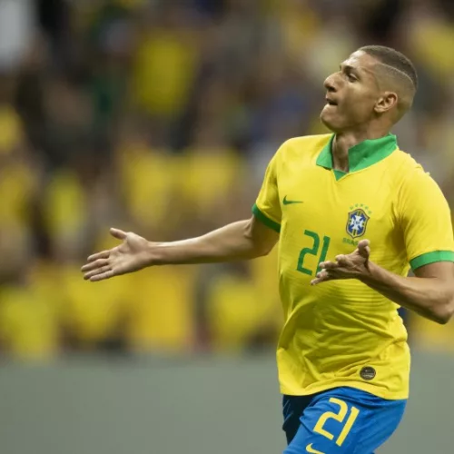 Jogador de futebol com número 21 e camiseta amarela da Seleção Brasileira comemora.