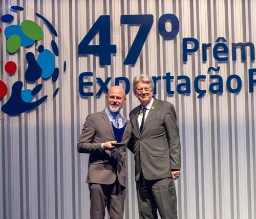 Dois homens de terno apertam as mãos em frente a letreiro 47º Prêmio Exportação