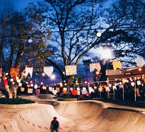 Uma pessoa em uma pista de skate à noite e, por cima, várias bandeirinhas juninas.