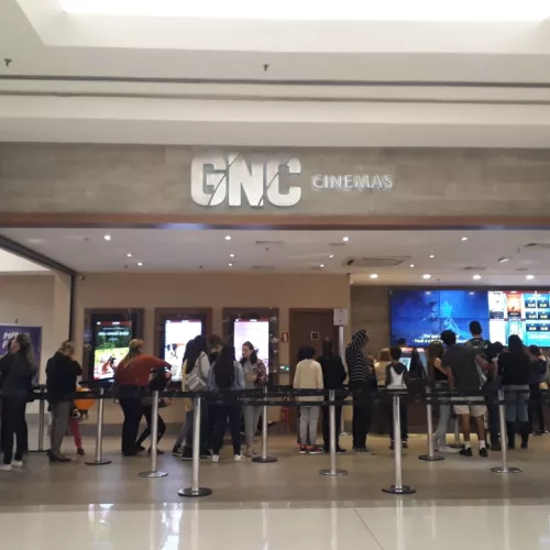 Frente do cinema com pessoas na entrada e esperando para comprar ingressos.