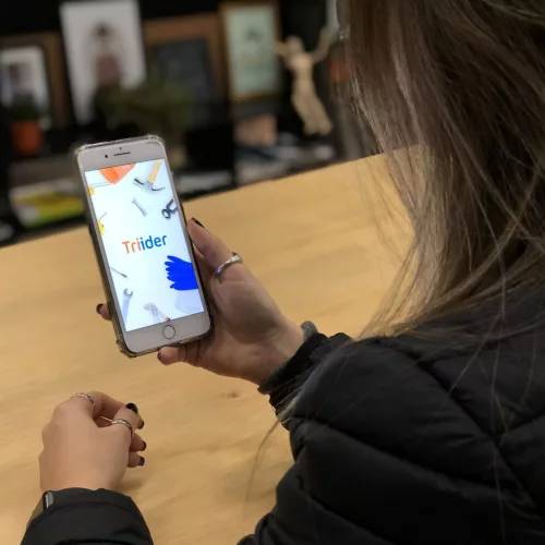 Um mulher utiliza um smartphone onde se vê acionado o aplicativo Triider.