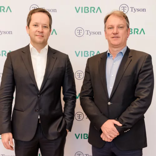Grupo Vibra e Tyson Foods. Dois homens de terno parados em frente a um painel com o nome das marcas Vibra e Tyson Foods.
