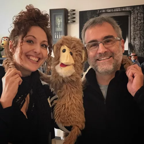 Uma mulher e um homem entre um boneco de macaco que parece abraçá-los.