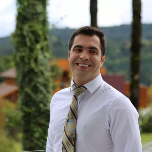 Michael Lopes D’Ávila. Um homem de camisa social e gravata sorri para a foto.