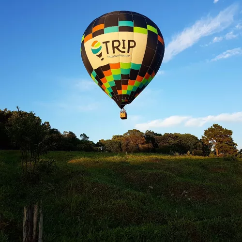 Balonismo. Um balão colorido com a inscrição "trip" sobrevoa um campo em um dia de céu azul.