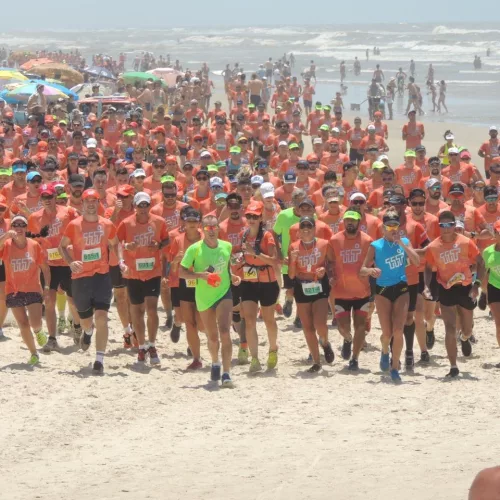 Centenas de atletas na areia da praia para a travessia.