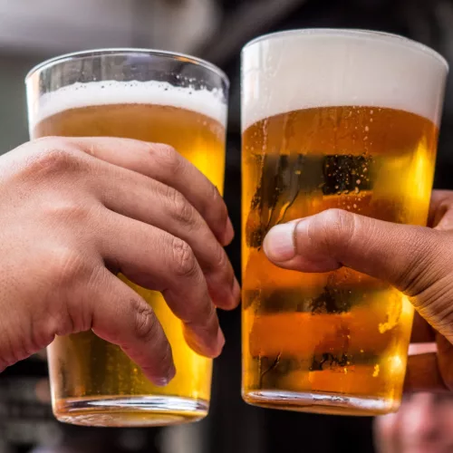 Cerveja convida a encontros reais. Duas mãos brindam com copos de cerveja