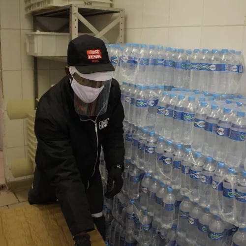 Coca-Cola, doação de água. Um homem usa máscara e separa garrafas de água.