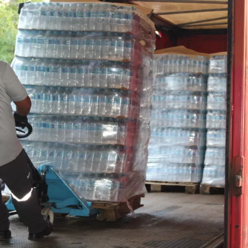 Coca-Cola, caminhão com garrafas de água. Um homem desloca garrafas em um carrinho.