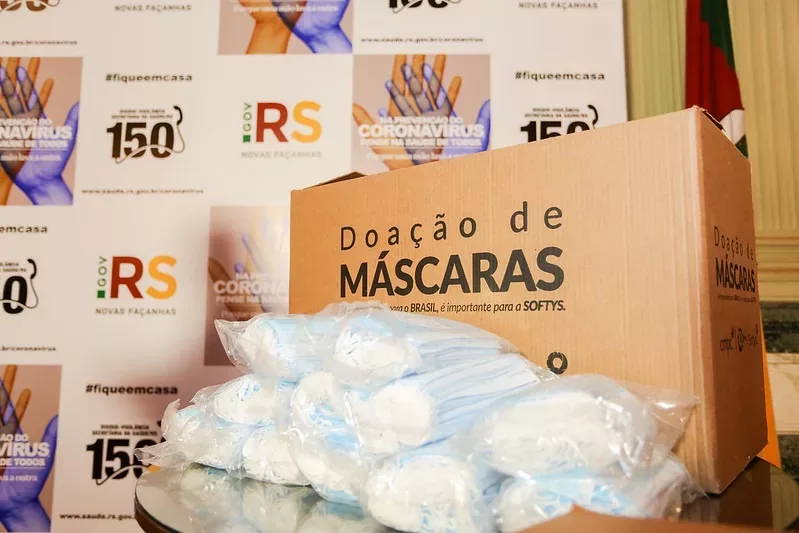 CMPC caixa com doação de máscaras e logos do governo ao fundo
