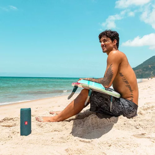 Gabriel Medina sentado com prancha de surf na praia e caixinha JBL