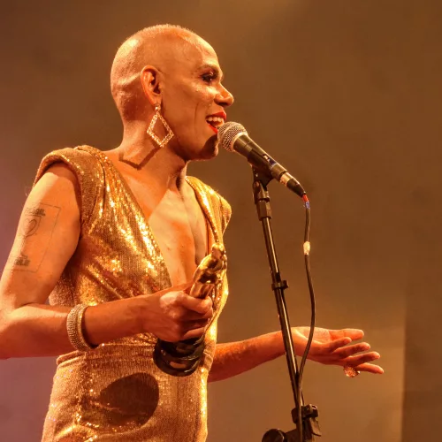 Uma pessoa careca cantando em um palco em frente a um microfone.