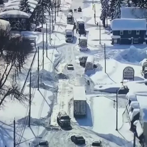 Imagem aérea mostra casas e uma rua cobertas por neve nos Estados Unidos. Vários carros estão parados por causa do volume de neve.