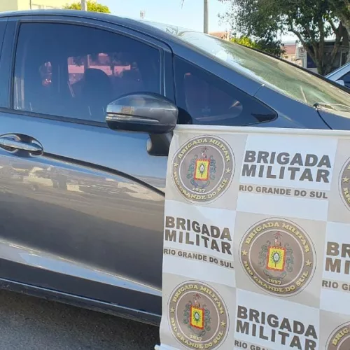 Banner com o logo da Brigada Militar é exibido em frente a veículo cinza apreendido em operação policial.