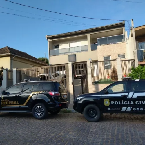 Dois carros pretos, um da Polícia Civil e um da Polícia Federal, em frente à uma residência. Agentes cumpriam mandados da Operação "O dobro ou nada".