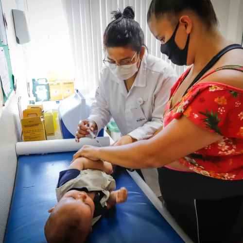 Bebê recebe de profissional de saúde e acompanhada da responsável, a aplicação de dose da vacina contra a covid-19