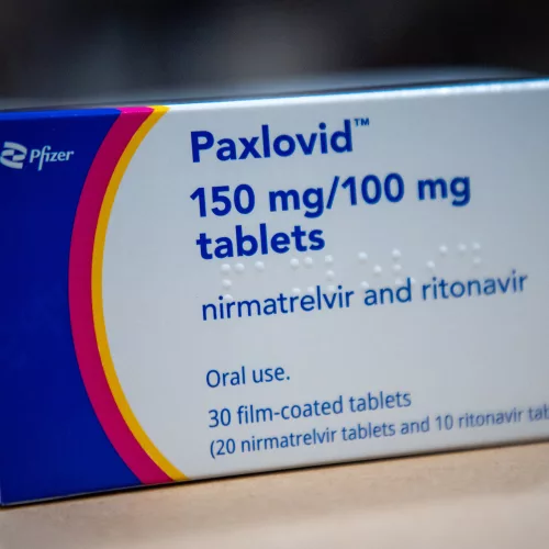 Caixa do medicamento Paxlovid, contra a Covid-19. Ela é branca, com letras e azul e uma faixa lateral em azul e outra em vermelho.