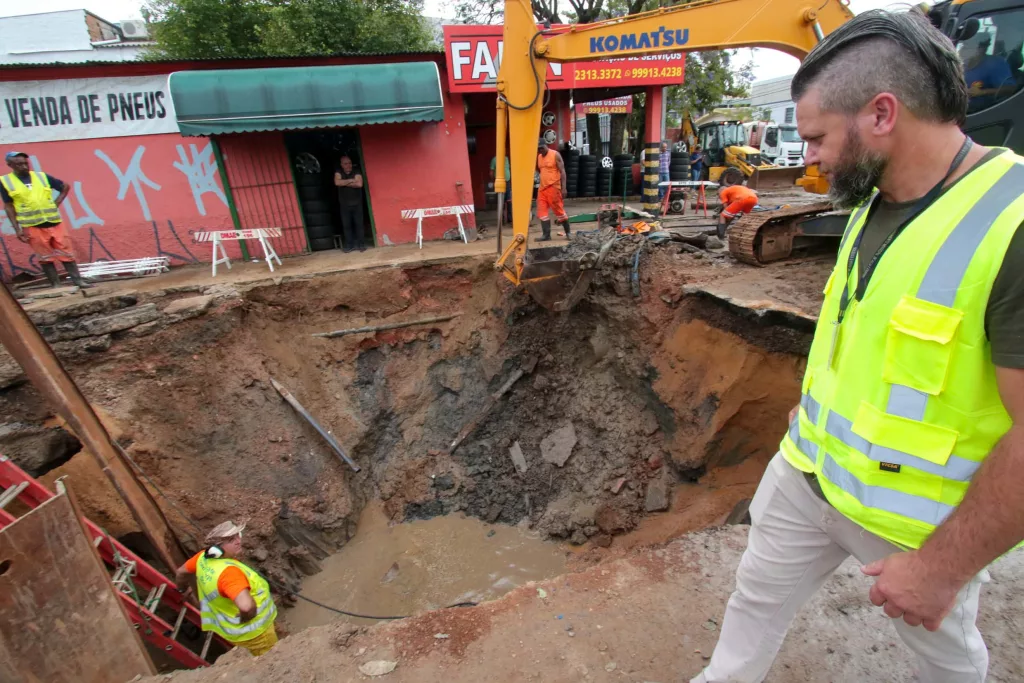Funcionário do DMAE vê retroescavadeira abrir buraco onde adutora se rompeu na avenida Sertório, em Porto Alegre.