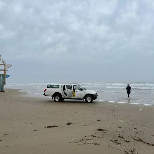 Imagem de um carro da Fepam em uma praia com uma pessoa saindo do mar com a coleta e água para análise do Projeto Balneabilidade 2023-2024.